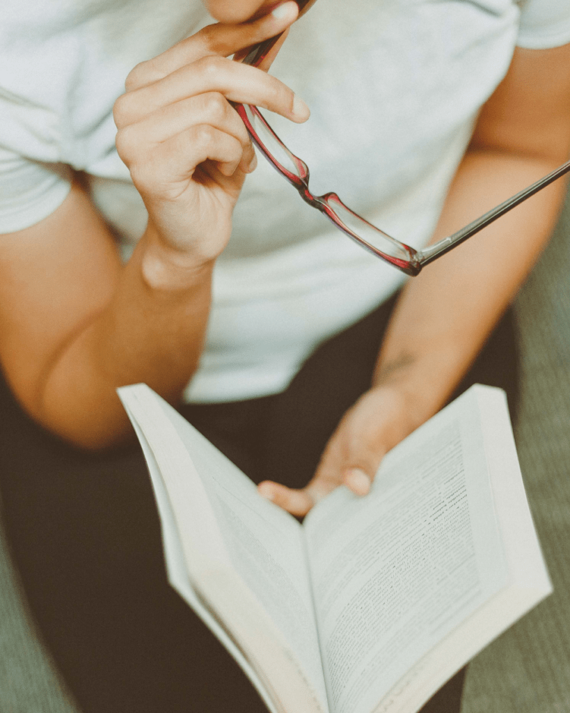 Hände halten ein aufgeschlagenes Buch, daneben eine Lesebrille
